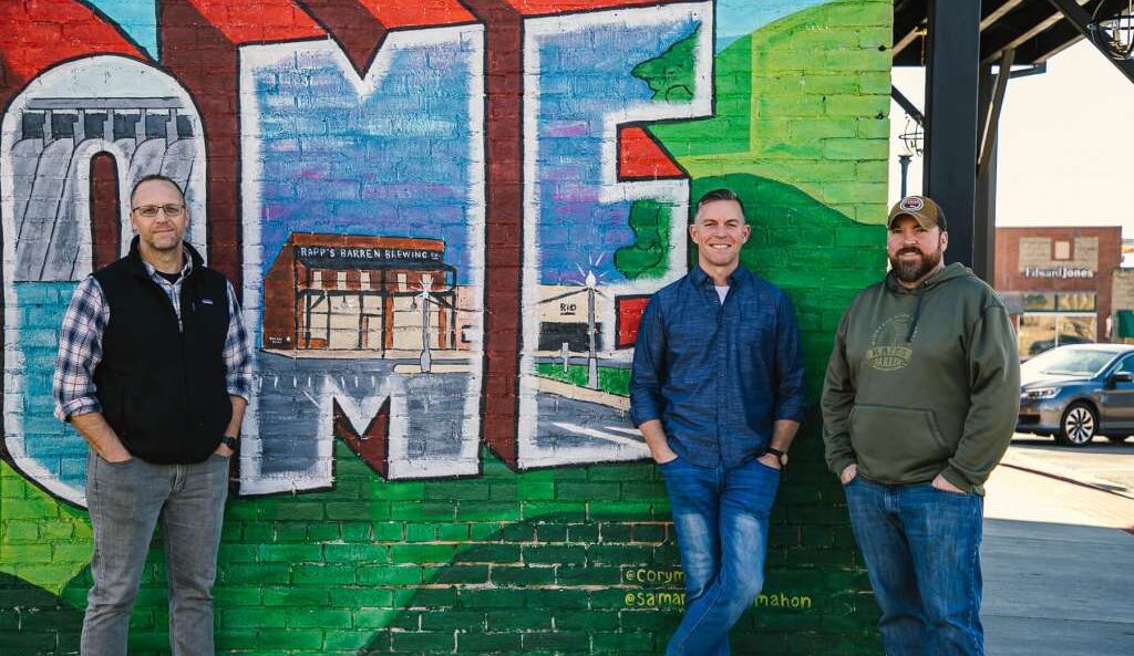 Three owners of Rapp's Barren Brewing Company in Mountain Home, Arkansas standing in front of a beautiful hand painted mural on the historic building.