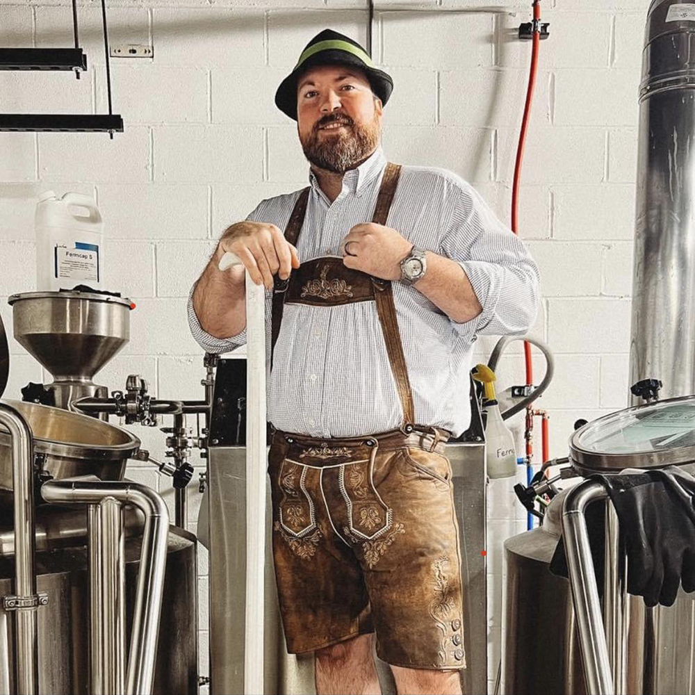 Head brewer dressed in full Octoberfest attire, standing proudly amongst the brewery equipment at Rapp's Barren Brewing Company in Mountain Home Arkansas